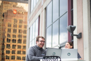 A male and female working on laptops in an outside workplace.